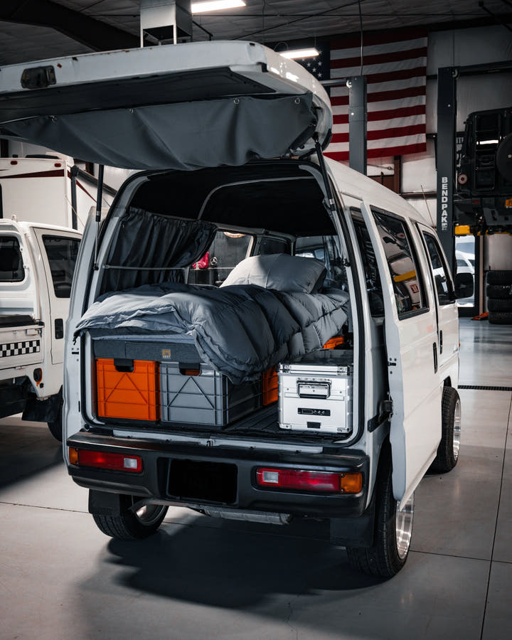 Gray SidioCrate storage system with orange bins and bedding inside a white camper van.