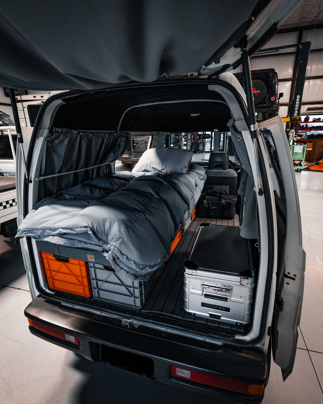 SidioCrate storage system with grey bedding and silver metal trunk inside a white camper van.