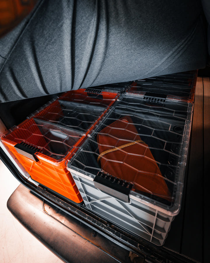 SidioCrate clear plastic storage bins with orange accents inside a camper van compartment.
