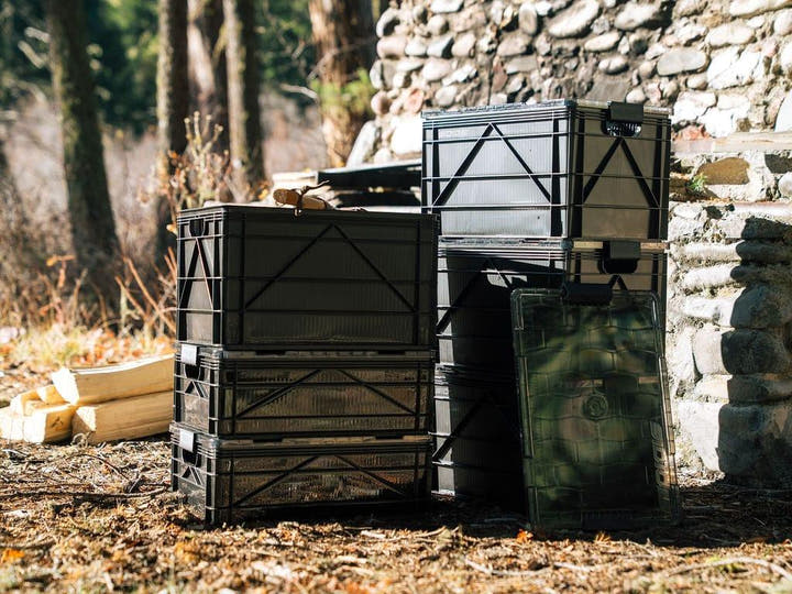 Stack of black SidioCrate storage containers for adventure vehicles in an outdoor setting.