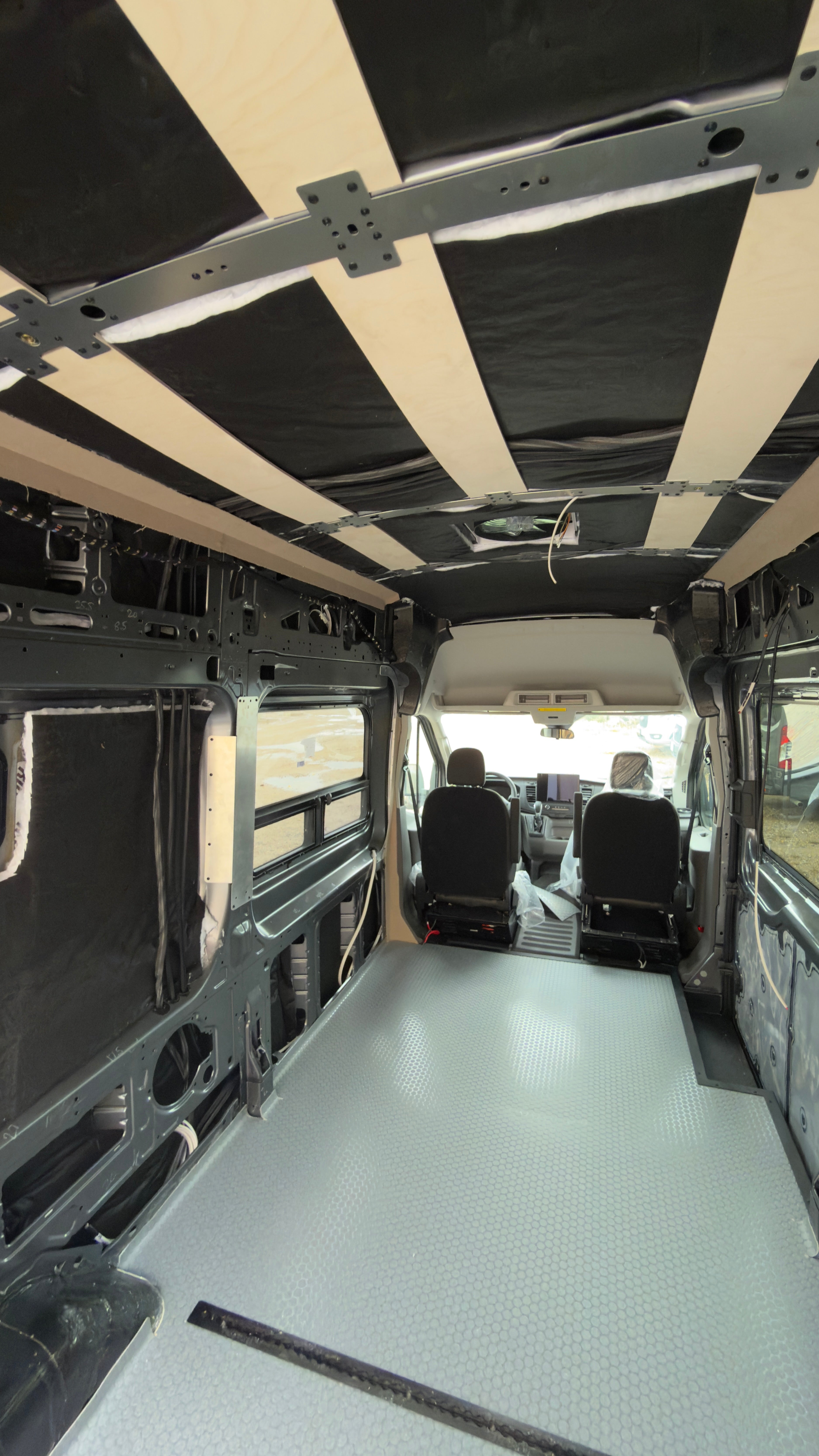 Cargo van interior mid-build with ceiling furring strips and gray floor