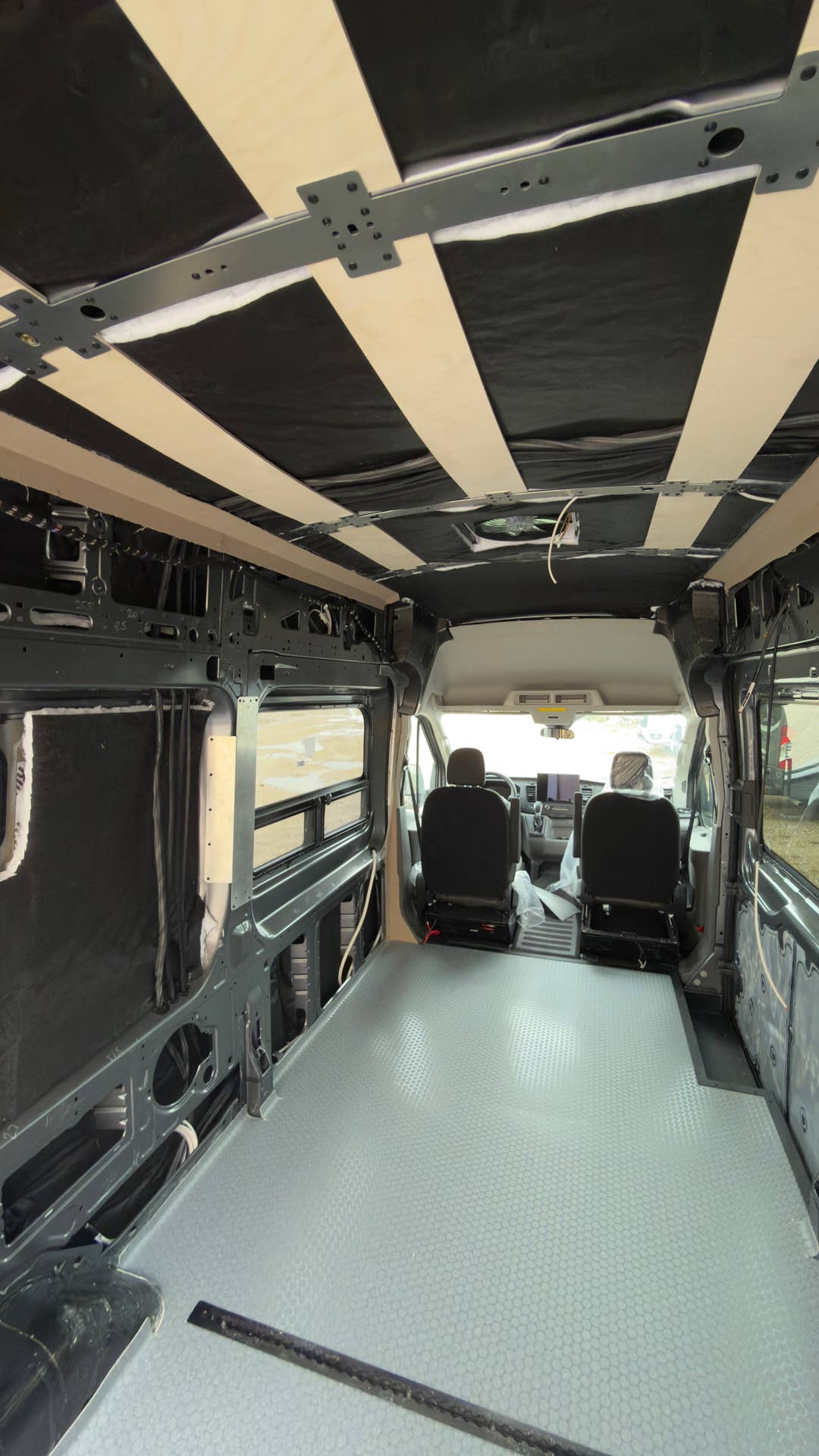 Cargo van interior mid-build with ceiling furring strips and gray floor