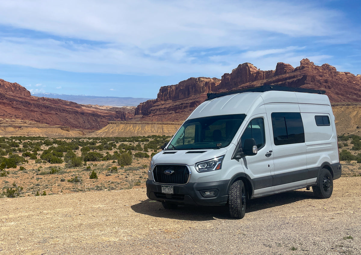 Silver Ford Transit camper van with roof rack parked in the desert