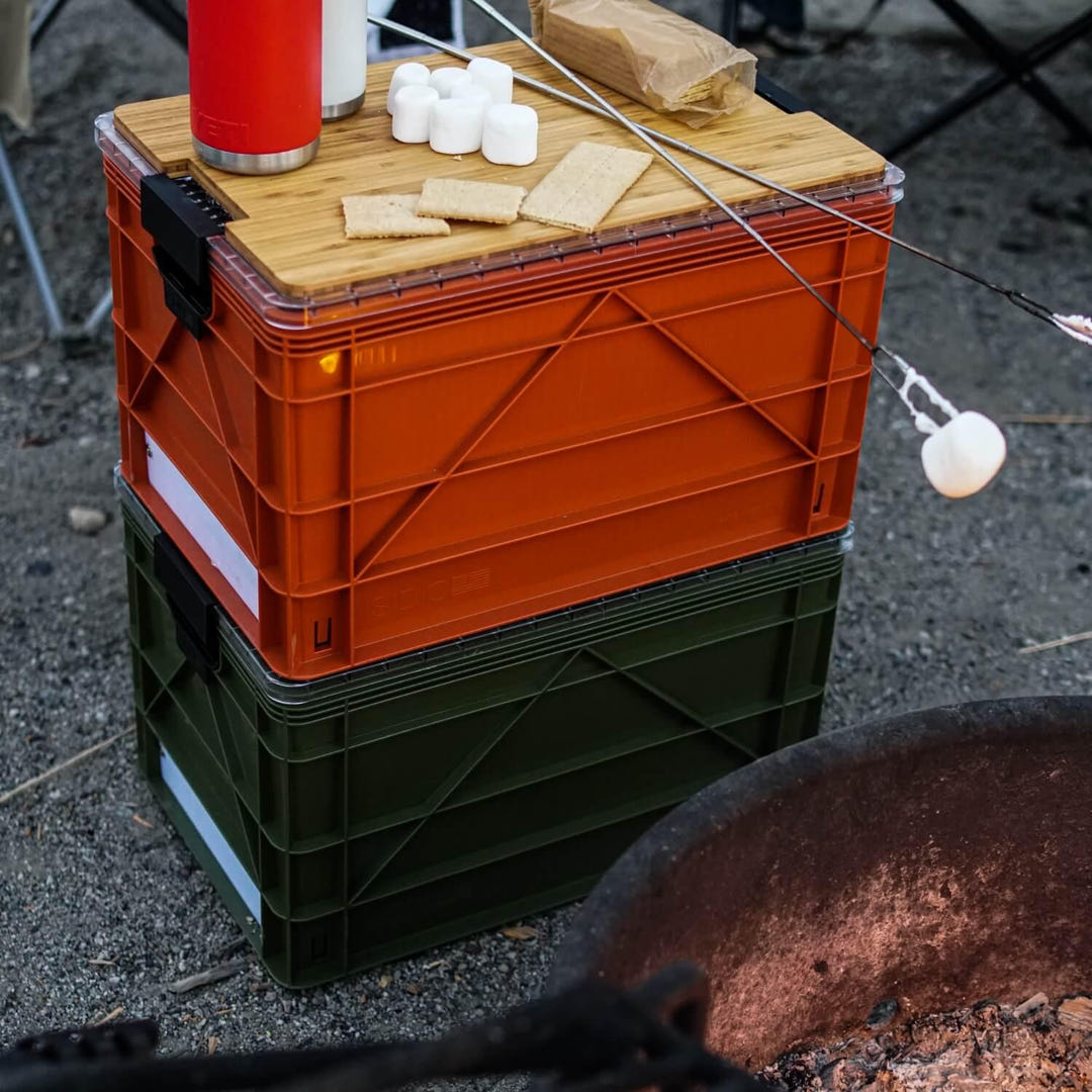 Stacked orange and green SidioCrate storage bins with a wooden lid used for camping food storage.