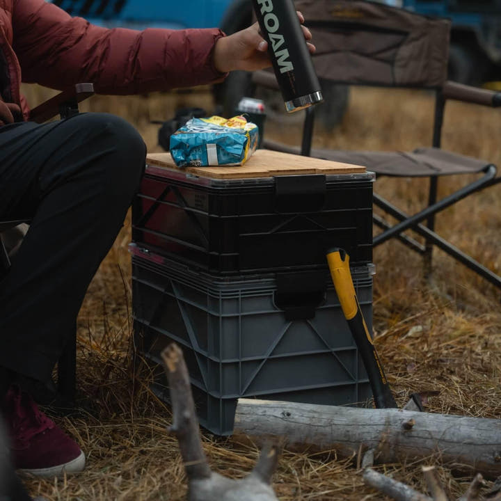 Stacked grey and black SidioCrate storage bins with a wooden top used as a table for camping.