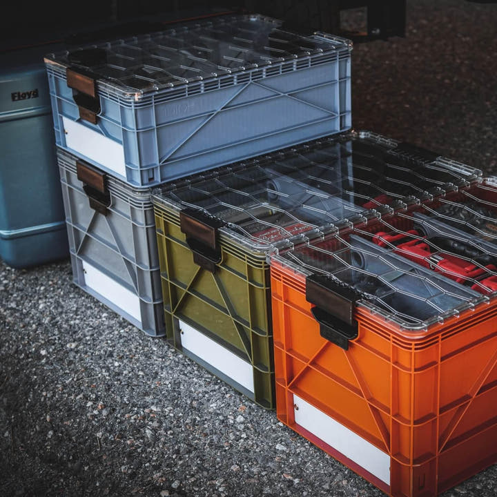 Stacked SidioCrate full size storage bins in grey, olive green, and orange with clear lids.