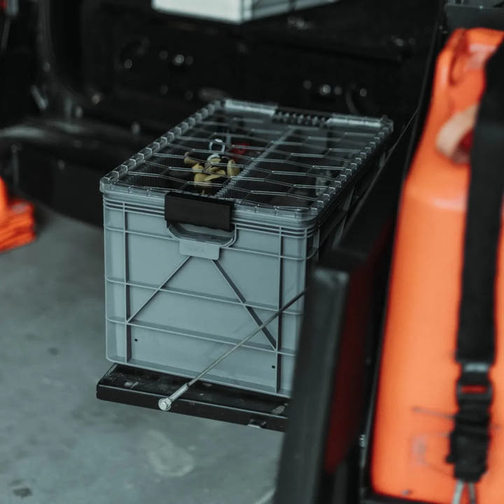 Grey SidioCrate storage bin with metal lid mounted on a black sliding tray in a camper van.