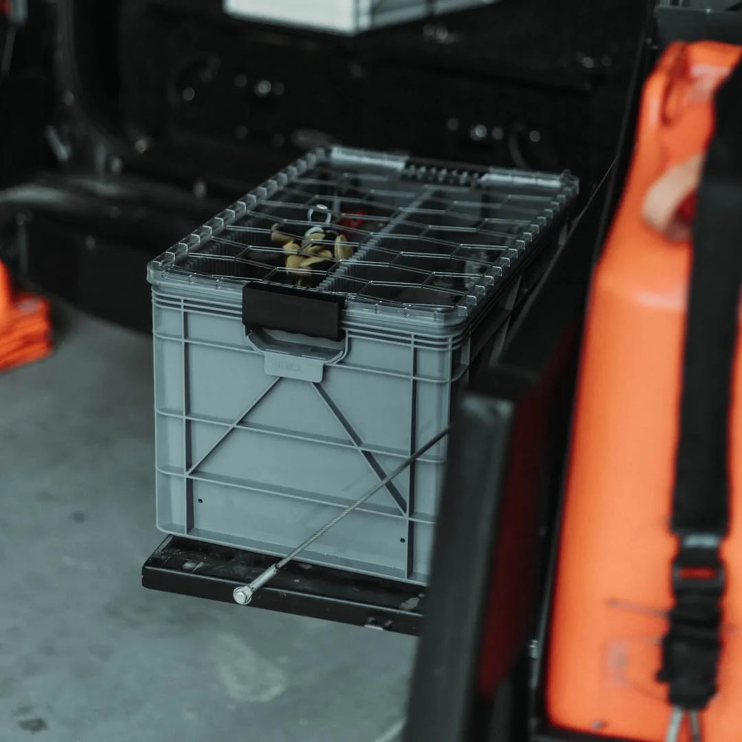 Grey SidioCrate storage bin with metal lid mounted on a black sliding tray in a camper van.